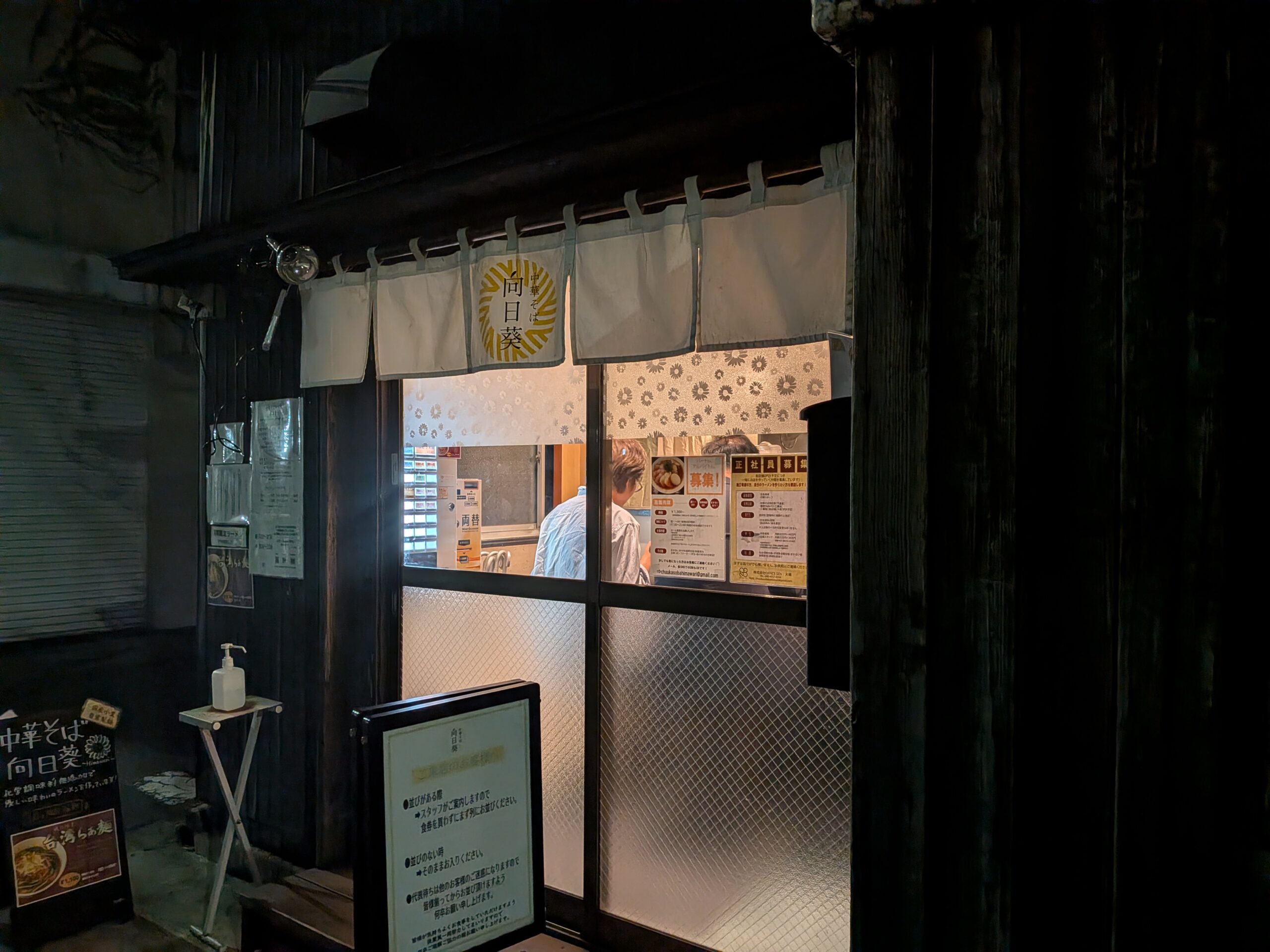 三鷹「中華そば向日葵」の店頭。中華そばと書かれた暖簾と食券機が見える入り口