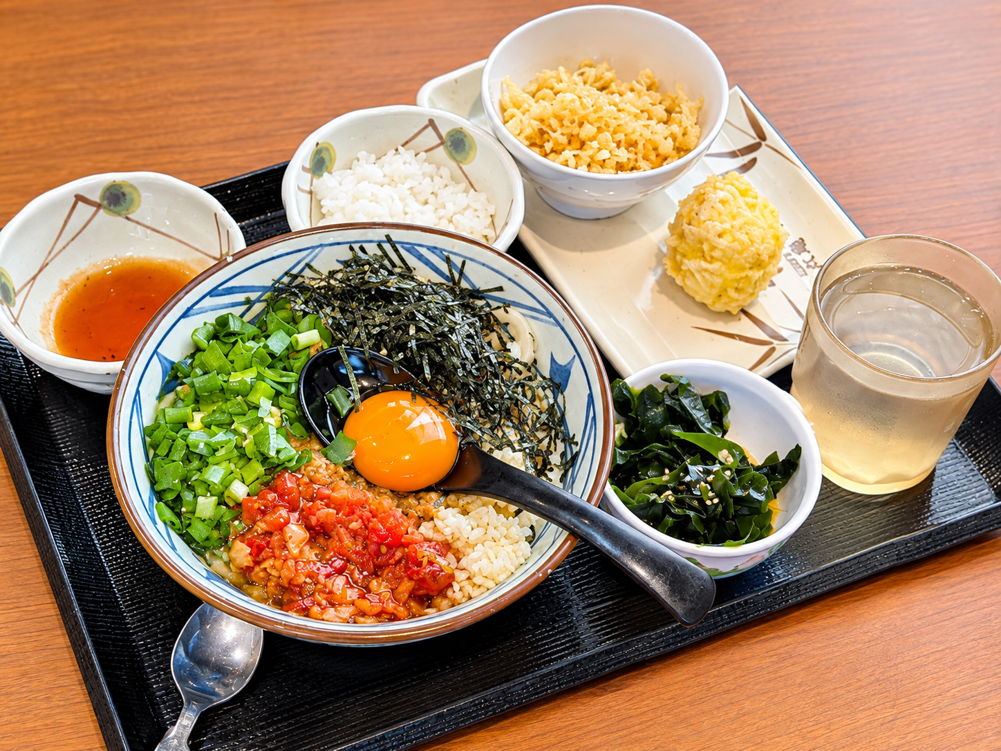 丸亀製麺 川崎多摩店で実食した期間限定「肉辛まぜうどん」。生卵・ネギ・ガリトマト・刻みのりをのせた状態